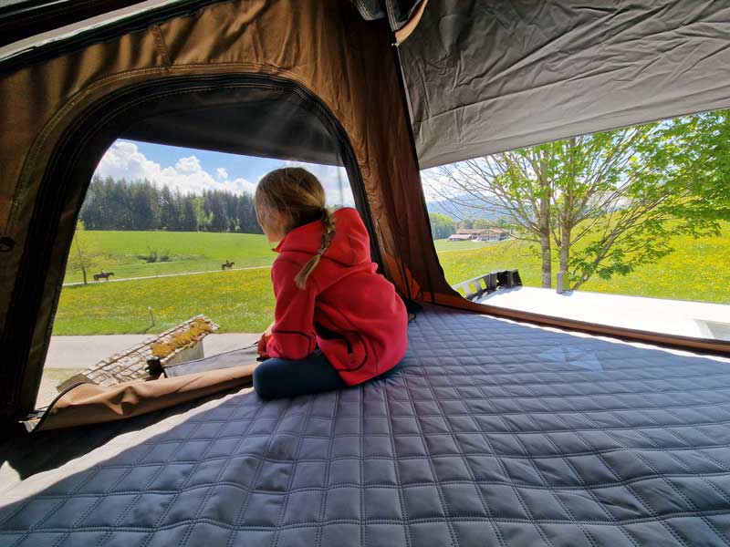 Wohnwagen mit Dachzelt Knd im sitzt im Dachzelt und genießt die Aussicht